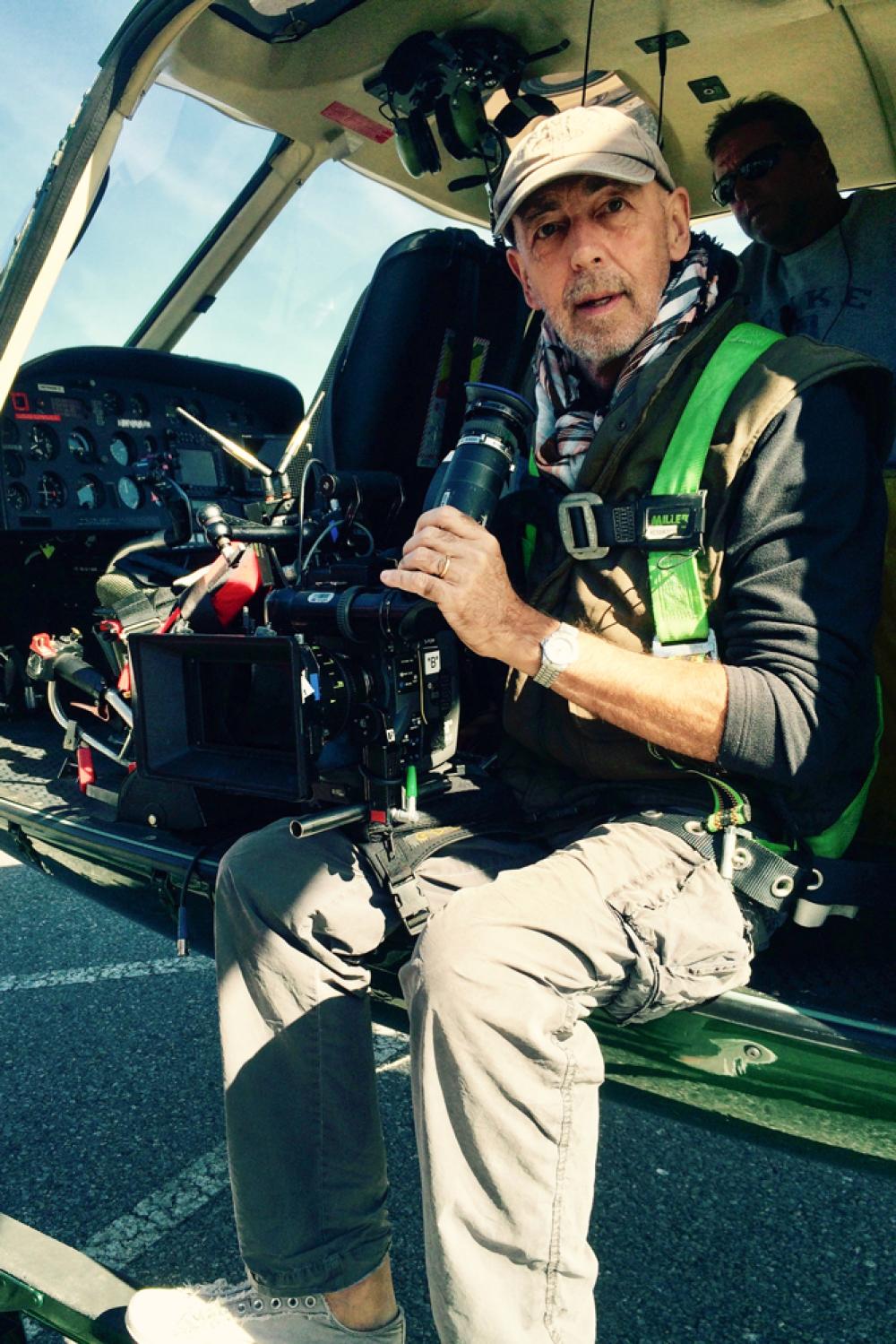 Stuart Dryburgh, holding a camera and sitting in a helicopter on the ground with its door open
