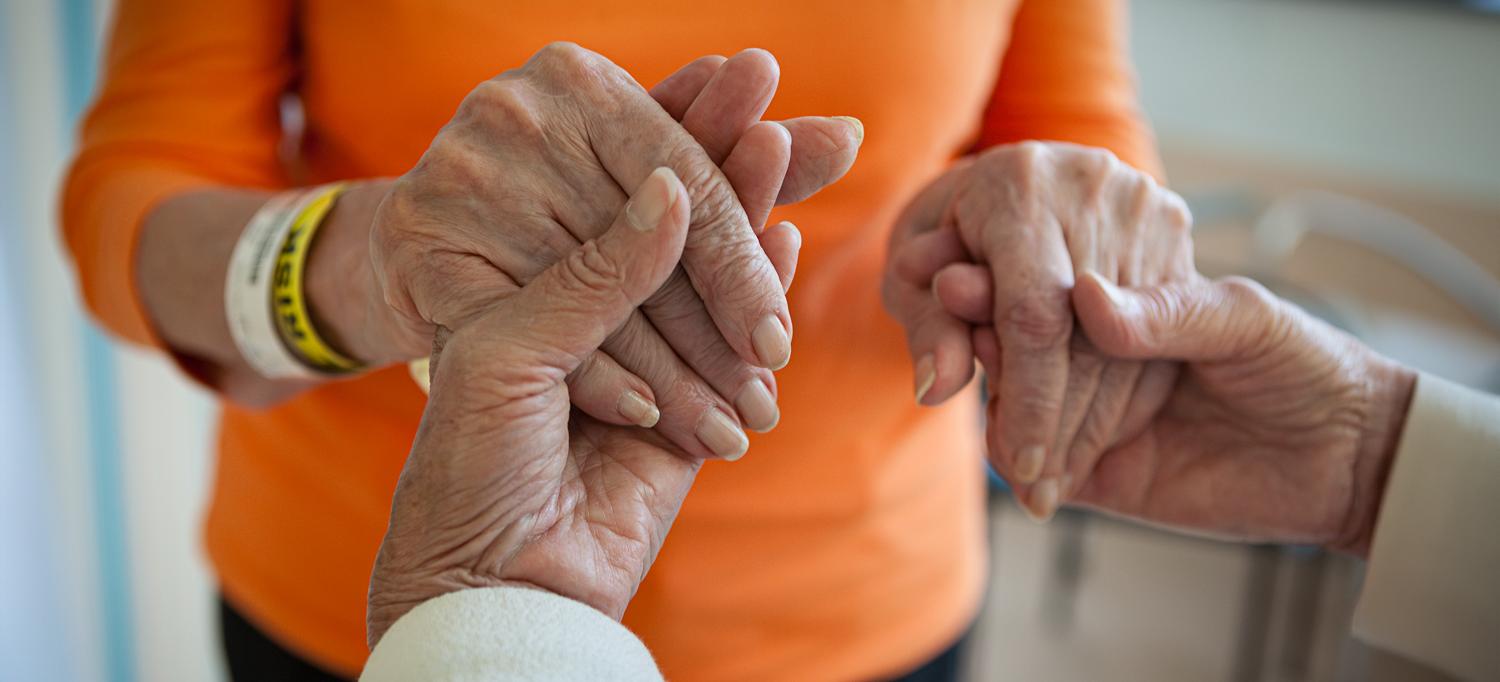 The hands of two older people embrace each other