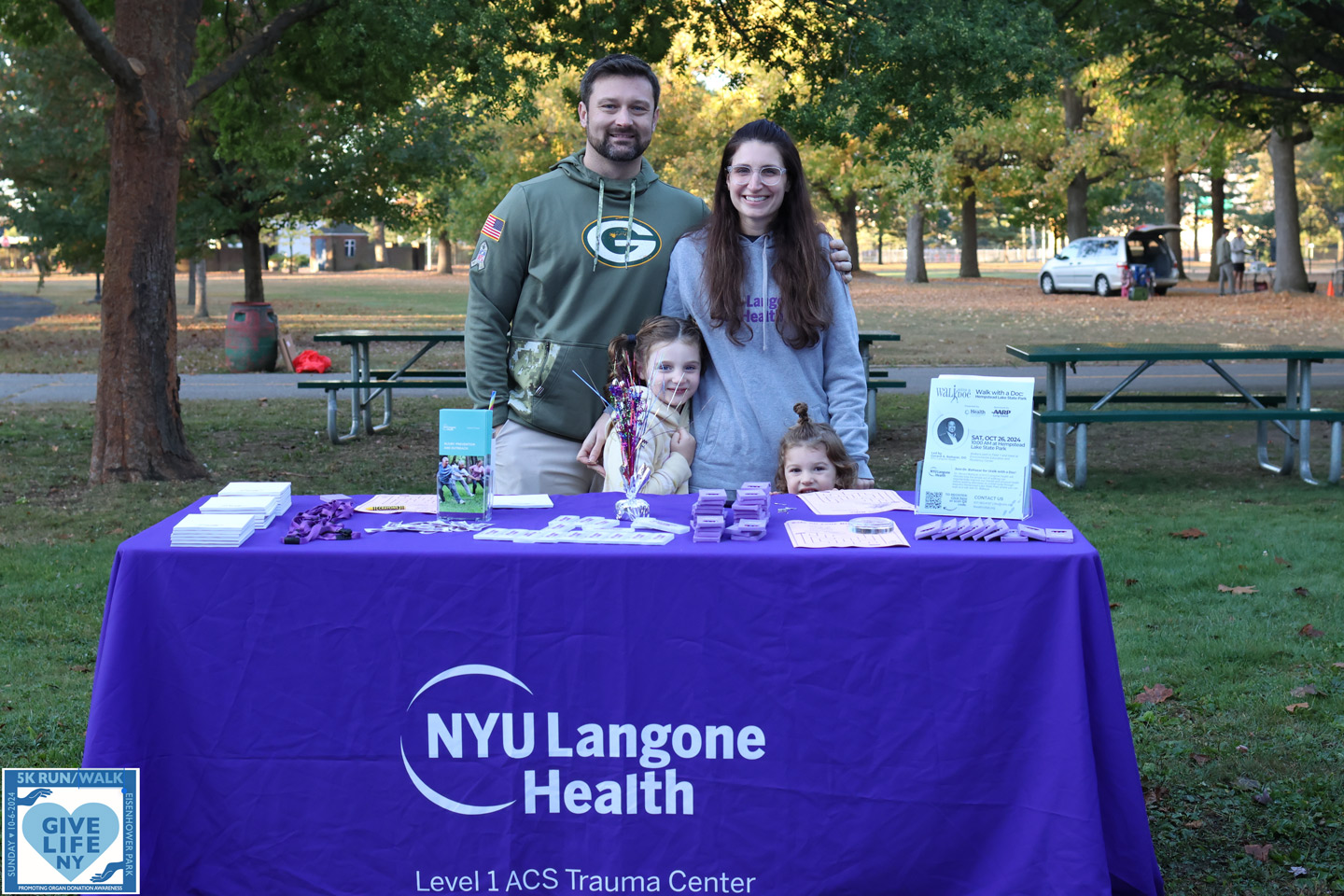 A man and woman with two small children stand behind a table that has NYU Langone Health Level 1 ACS Trauma Center branding.