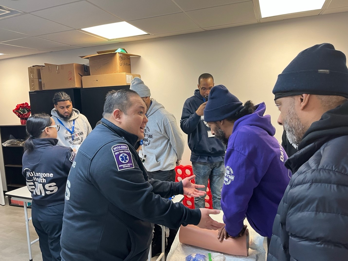An NYU Langone instructor guides a group during a hands-on training session, as one person practices on a simulation model.