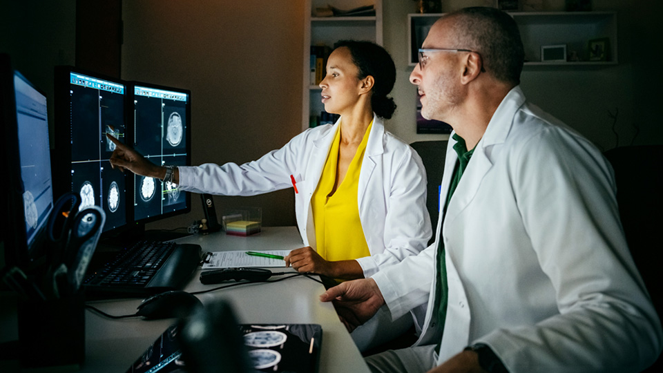 Two medical professionals review a CT scan on a monitor.