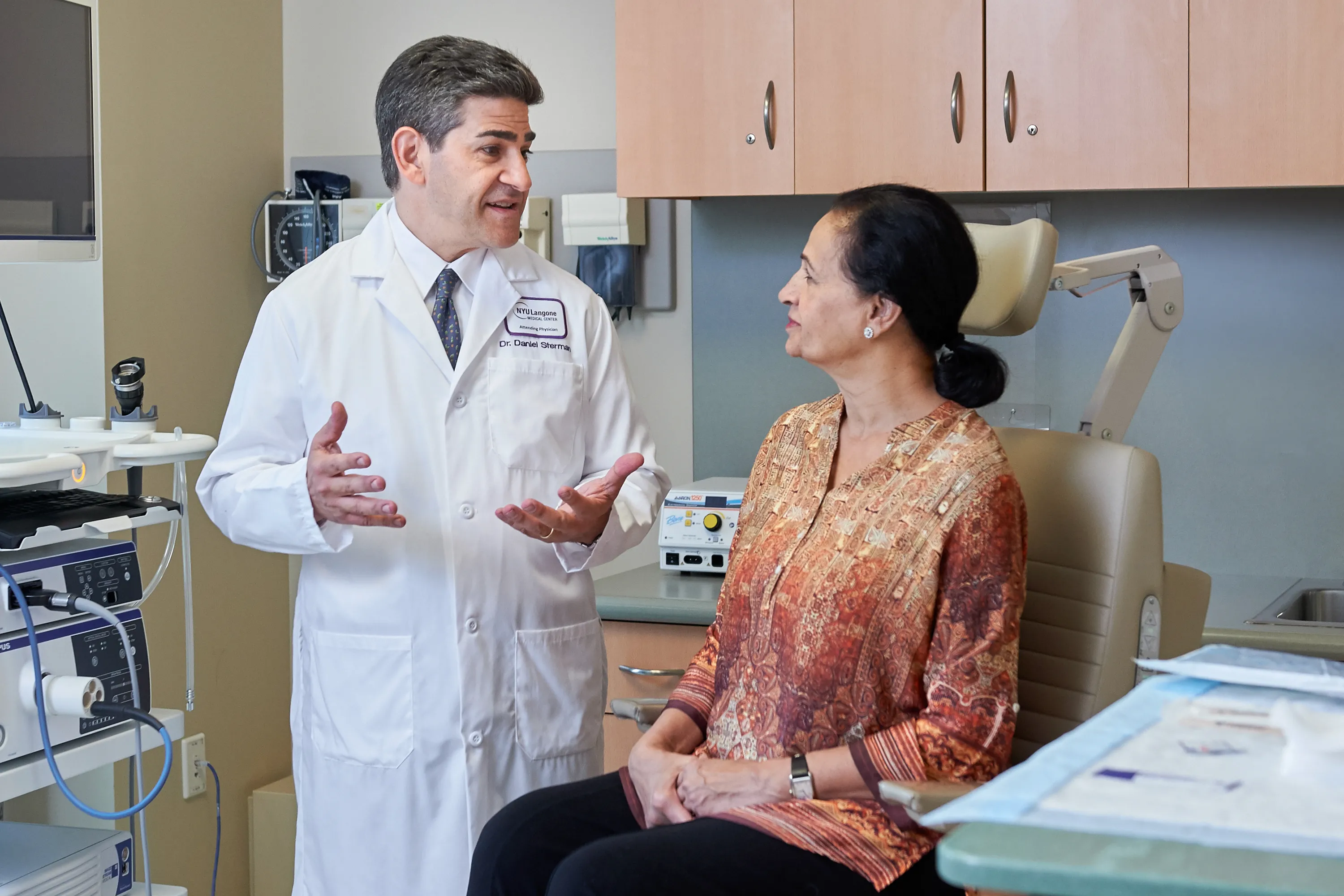 Dr. Daniel Sterman gestures with his hands as he talks to a patient sitting on an exam table.