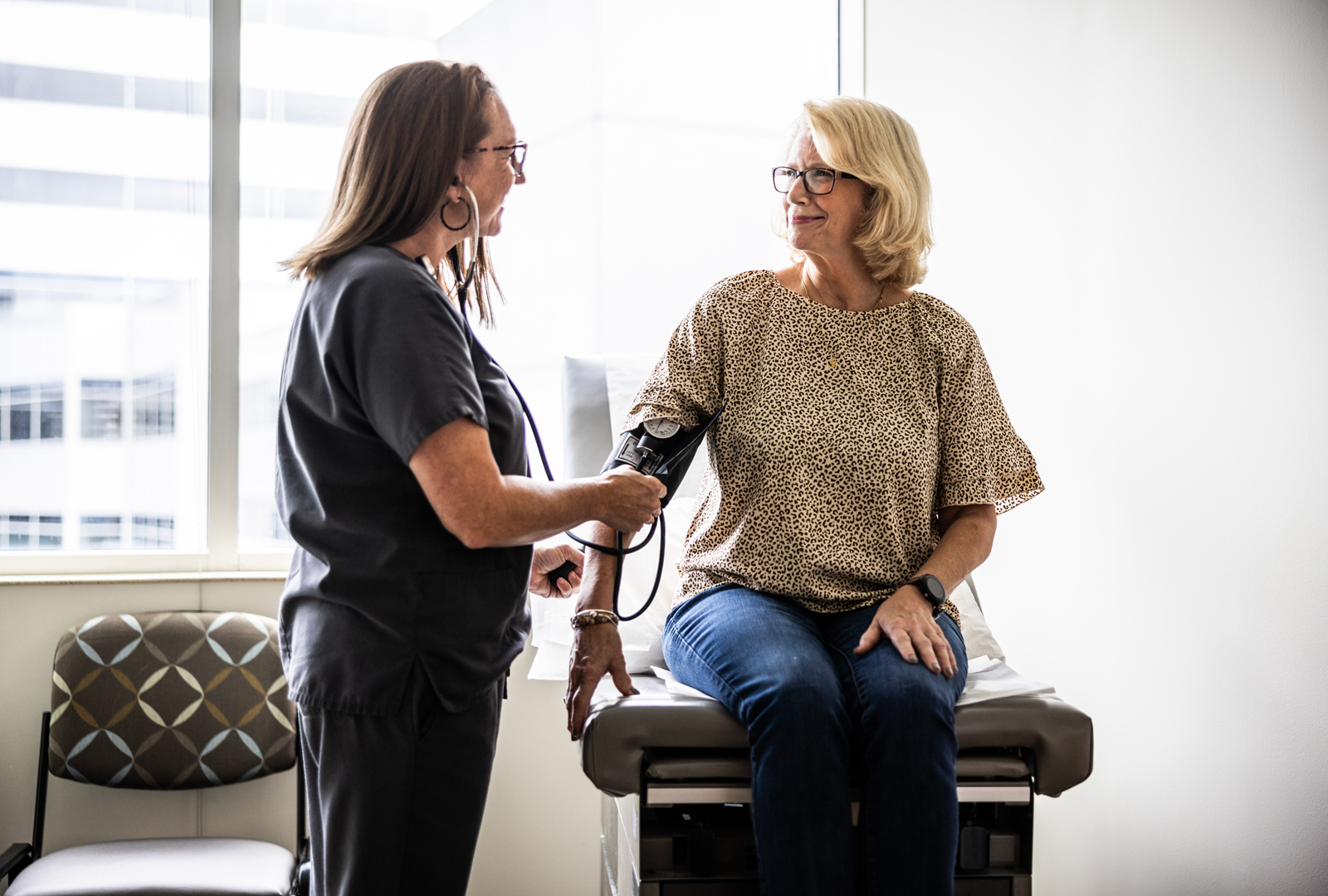 A health provider takes a woman’s blood pressure while she sits on an exam table.