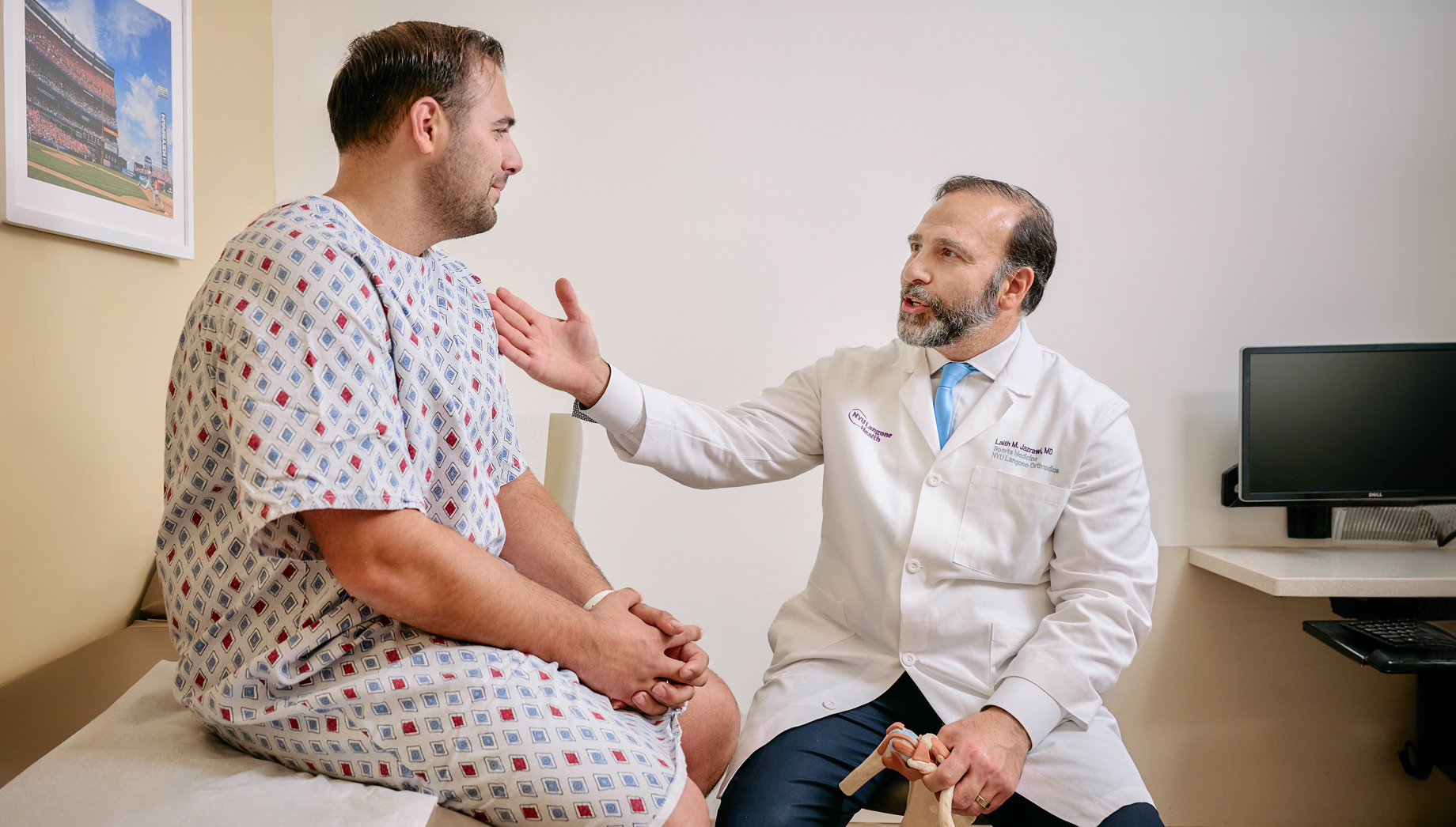 Dr. Laith M. Jazrawi talks to a patient wearing a medical gown and sitting on an exam table.