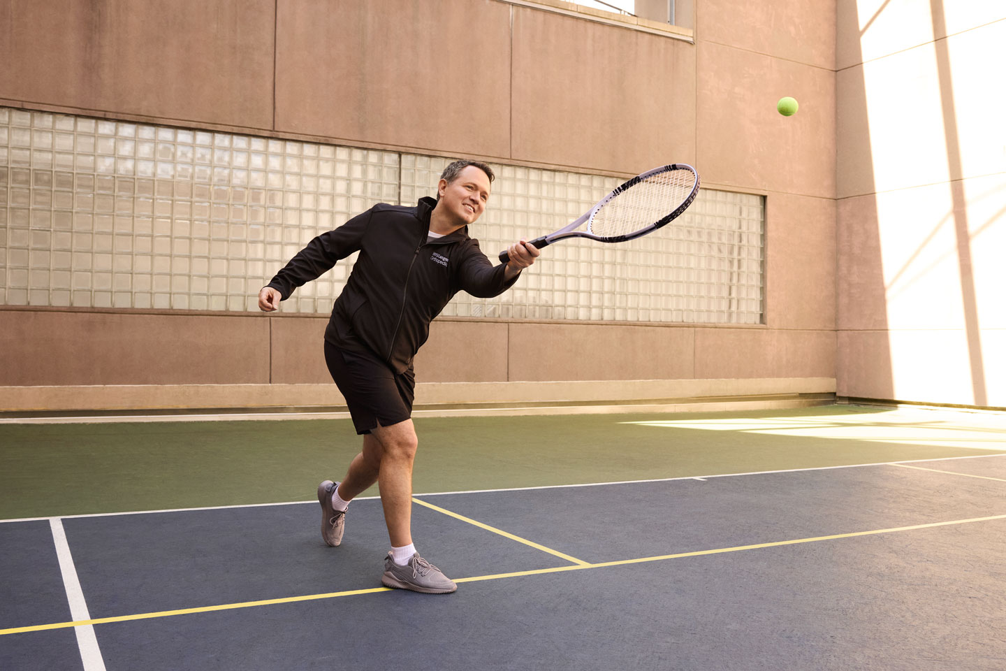 Dr. Matthew Hepinstall follows through on hitting a tennis ball with a racquet on a tennis court