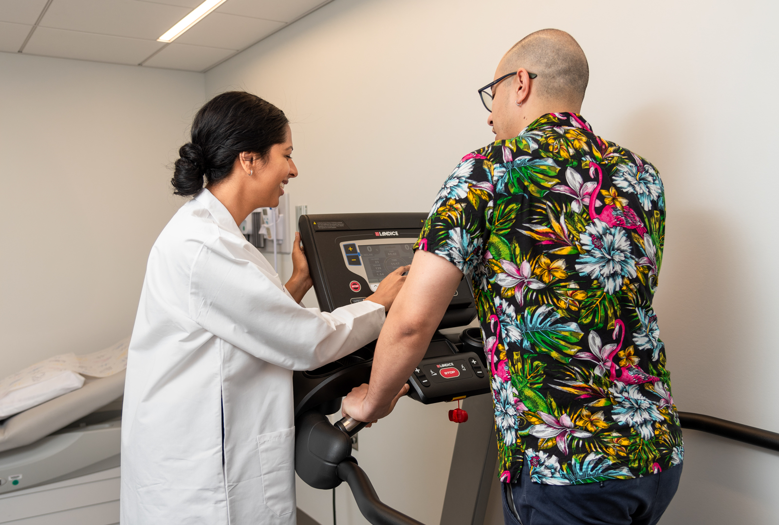 Physician assistant Swathi Bolneni adjusts the controls of a treadmill that a patient is walking on.