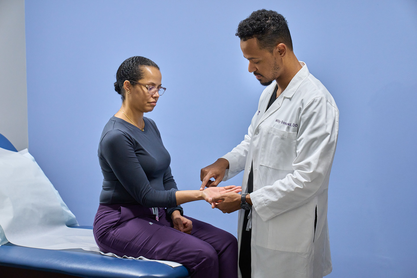 Dr. Willy Gonzalez examines the wrist of a patient who is sitting on an exam table.