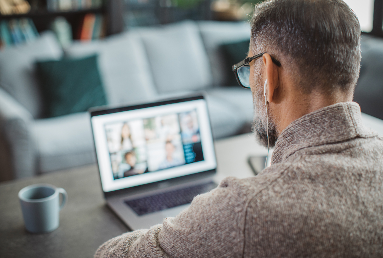 A man wearing earbuds sits at a desk while listening to a webinar at home.