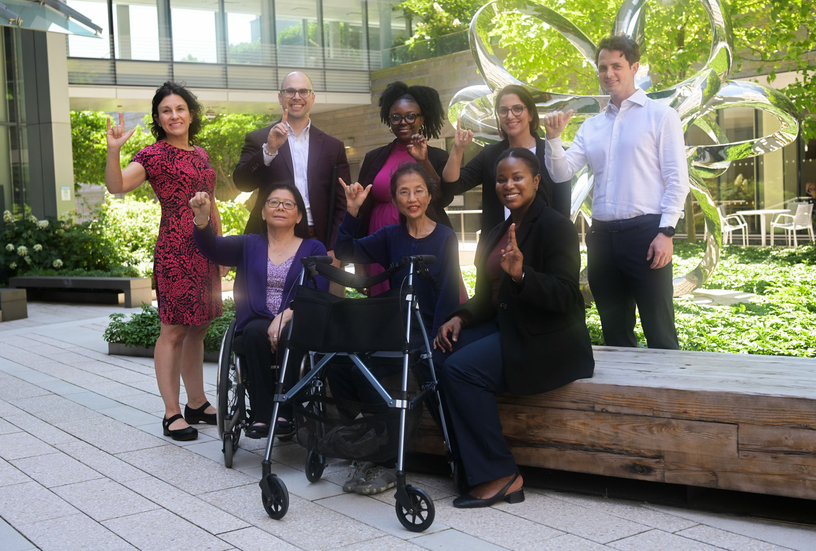 A group of people sitting and standing in an outdoor courtyard, using American Sign Language (ASL).