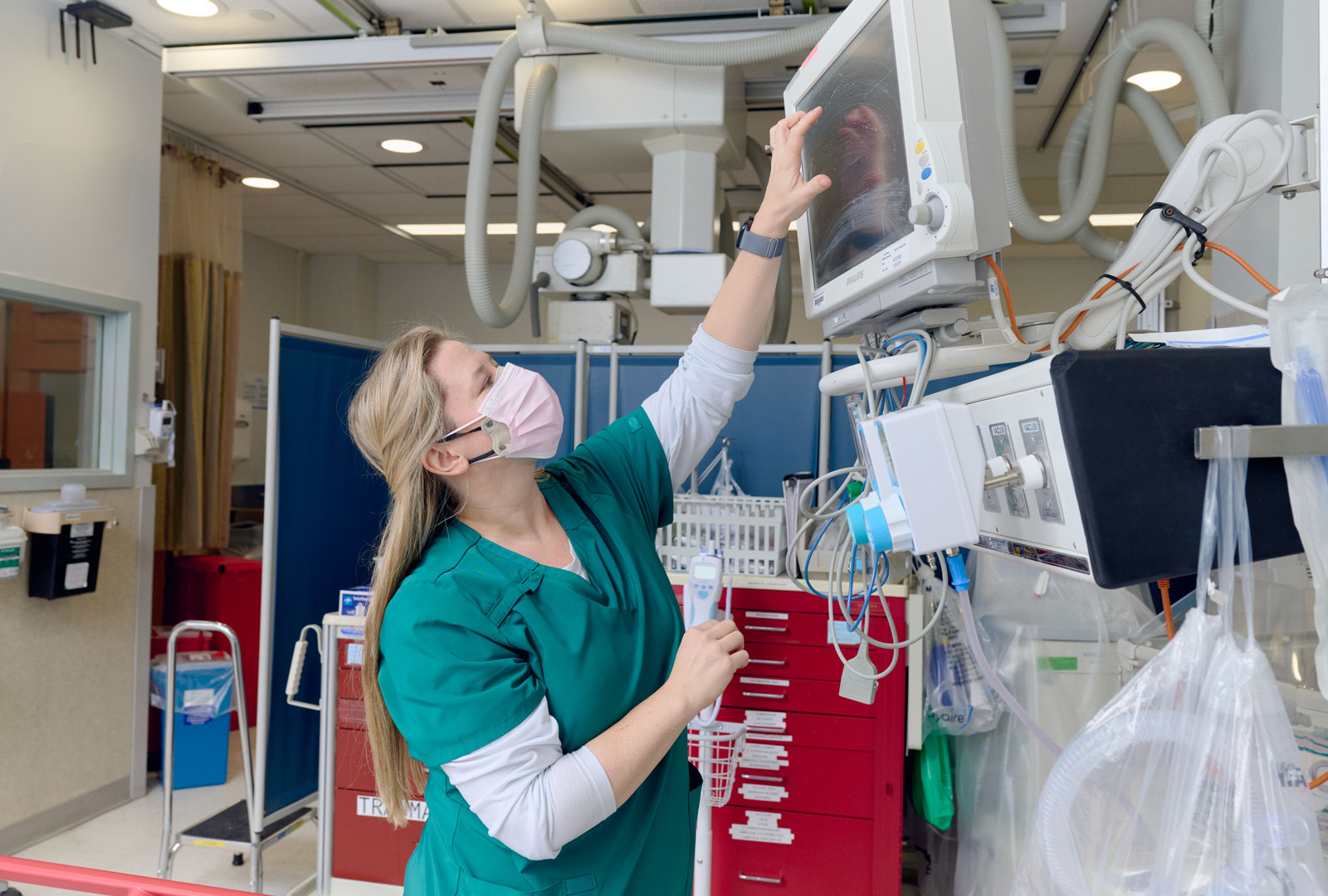 A healthcare provider adjusts a medical monitor in hospital trauma care unit.