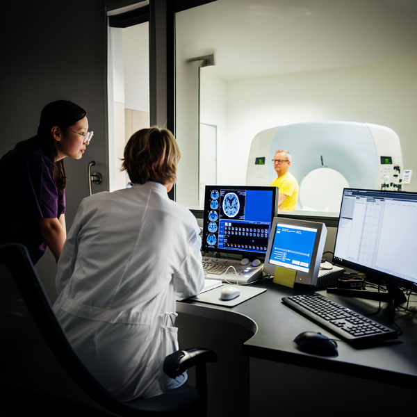 Two providers reviewing imaging results on a computer screen, as person in the imaging room looks in on them