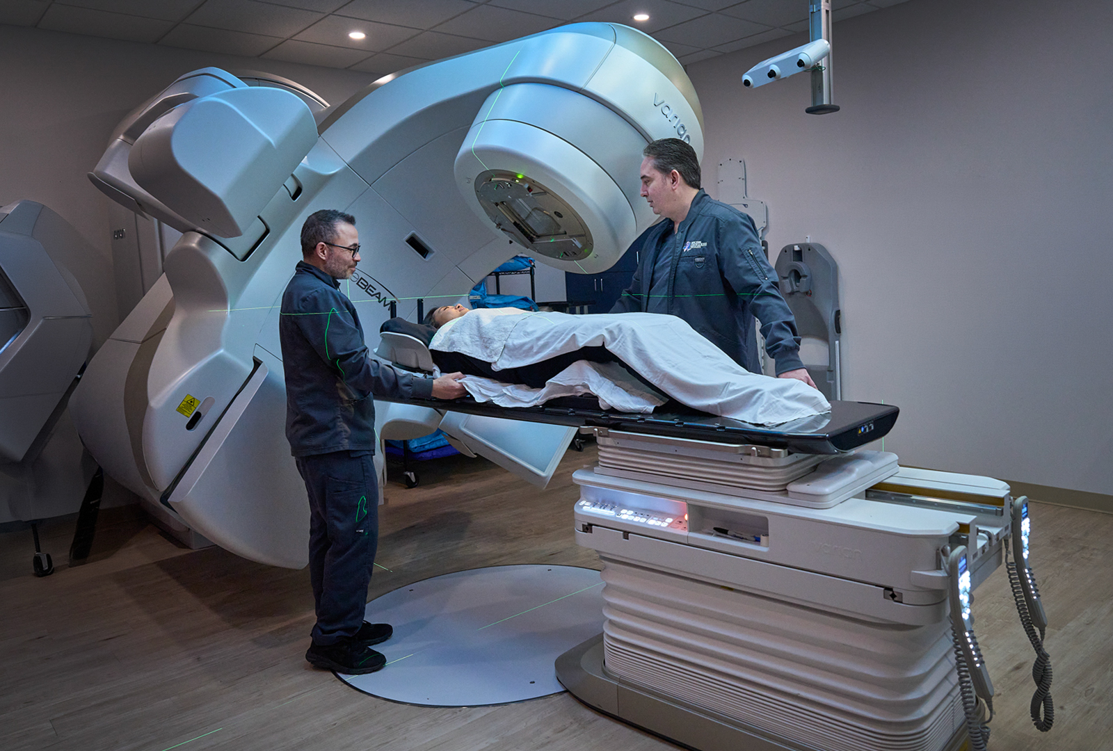A patient lies on his back while being treated in a procedure room, as two providers stand nearby.