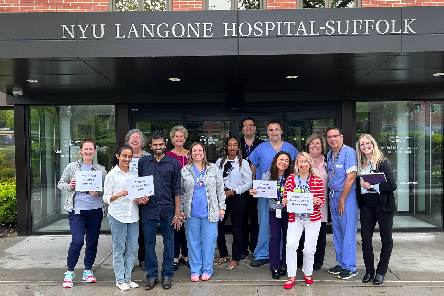 Healthcare providers stand together outside NYU Langone Hospital—Suffolk holding signs supporting Trauma Survivors Day.