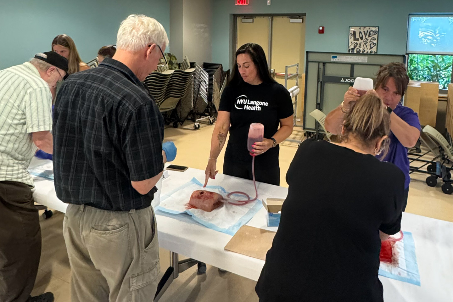 People practice a wound care simulation as an NYU Langone Health instructor demonstrates using a model with tubing and fluid.