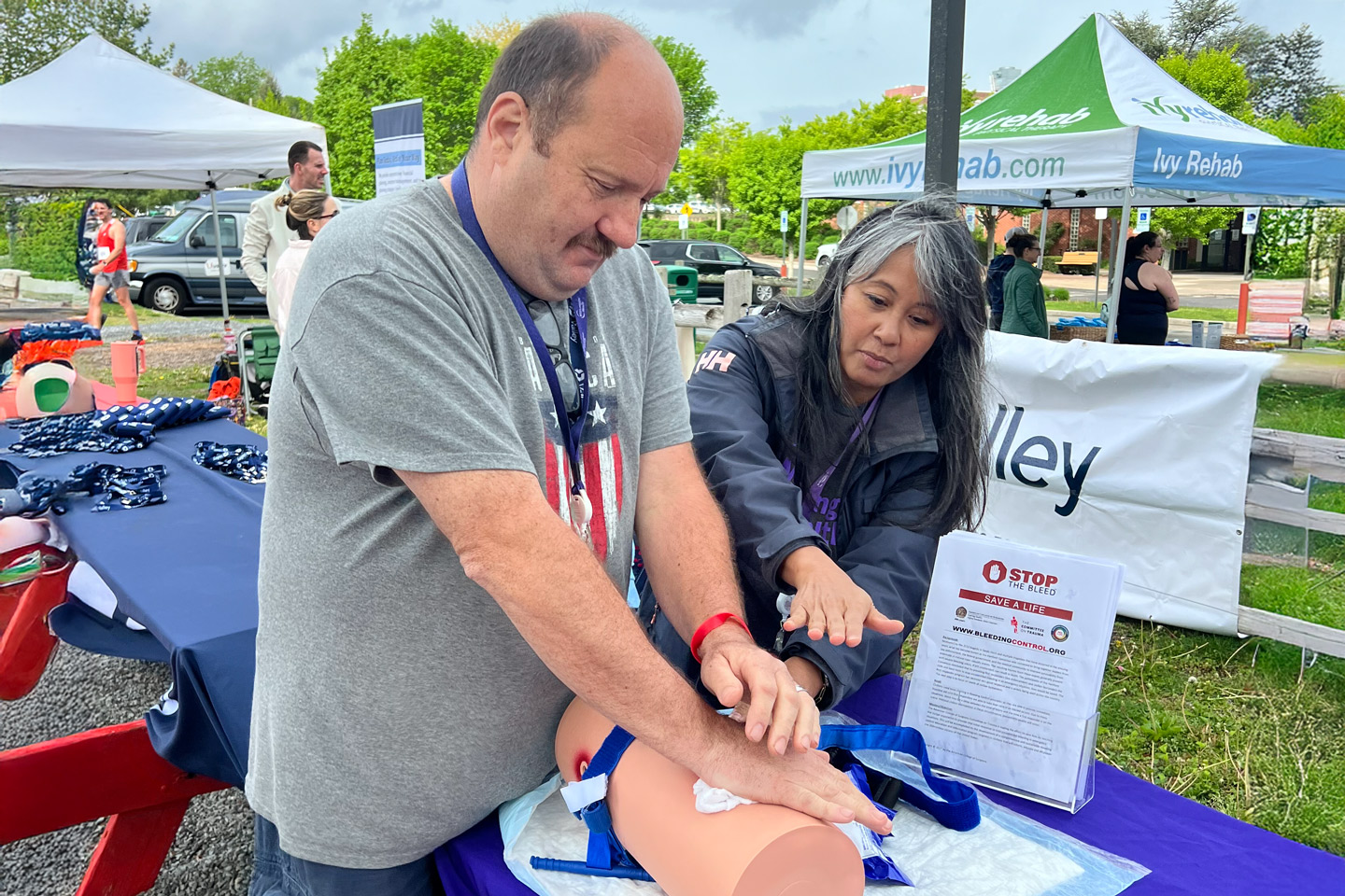 A man practices wound care on a training mannequin with guidance from an instructor during a Stop the Bleed event.
