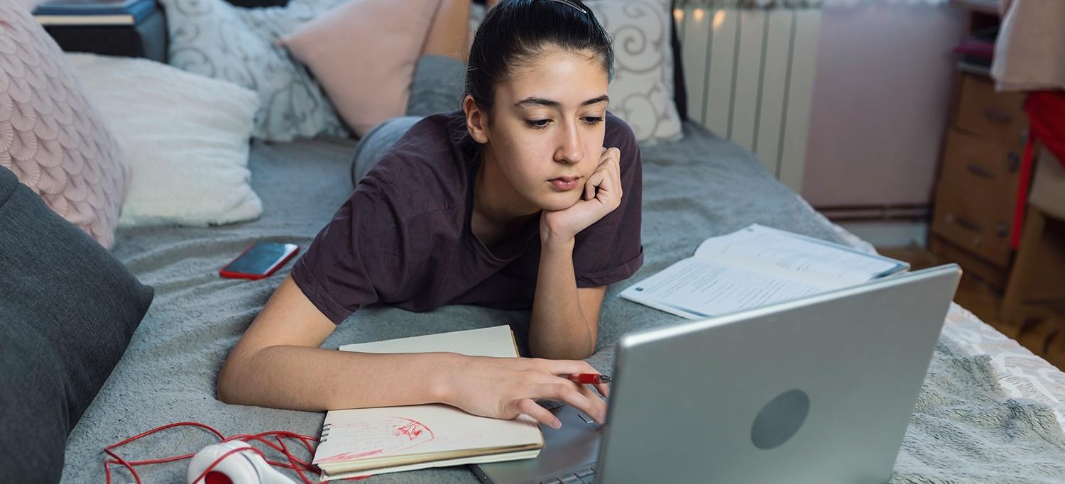 Teen Working on Laptop Computer from Bed