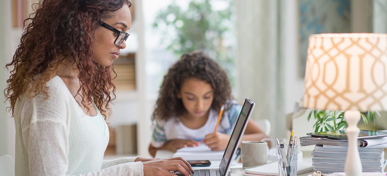 Woman Working on Laptop Computer While Child Does Homework