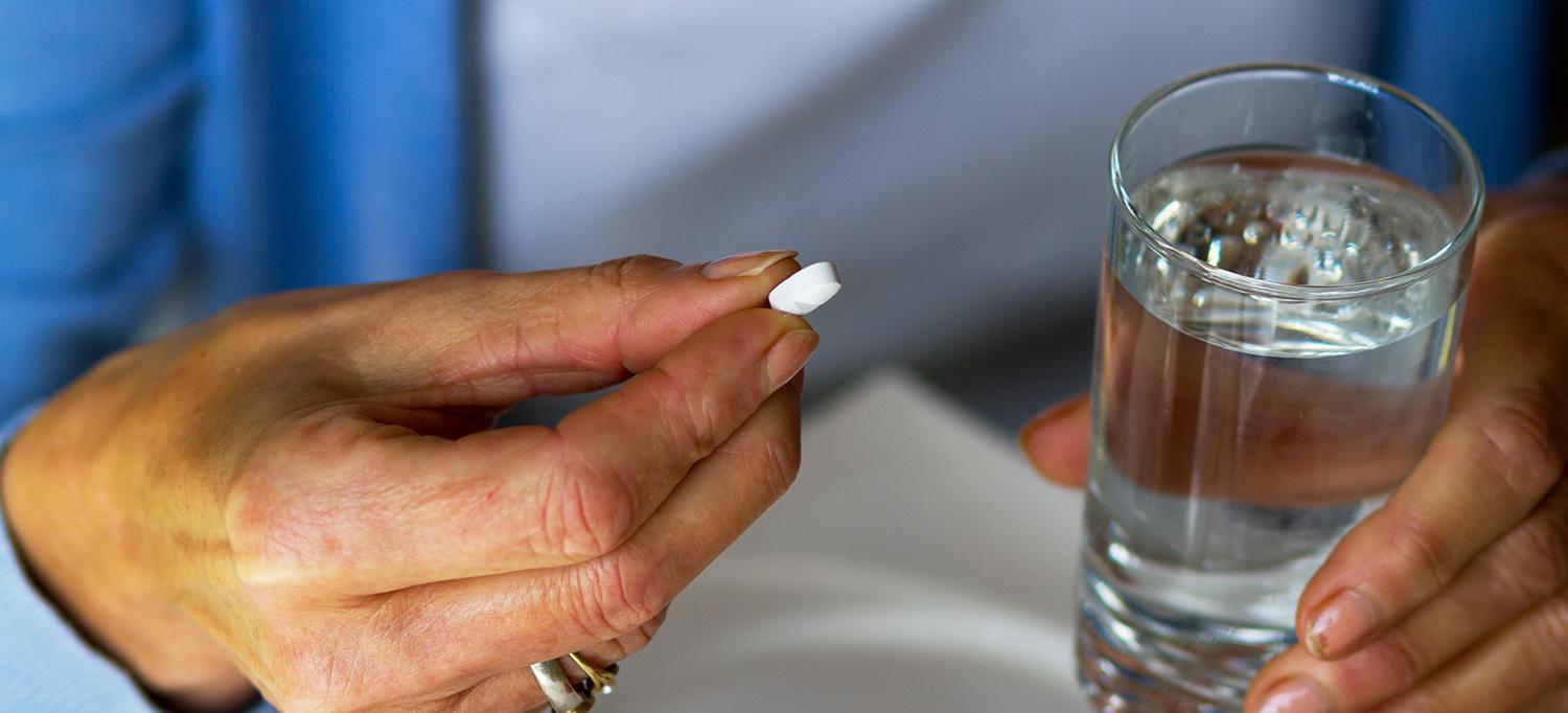 Person Holding Pill and Glass of Water