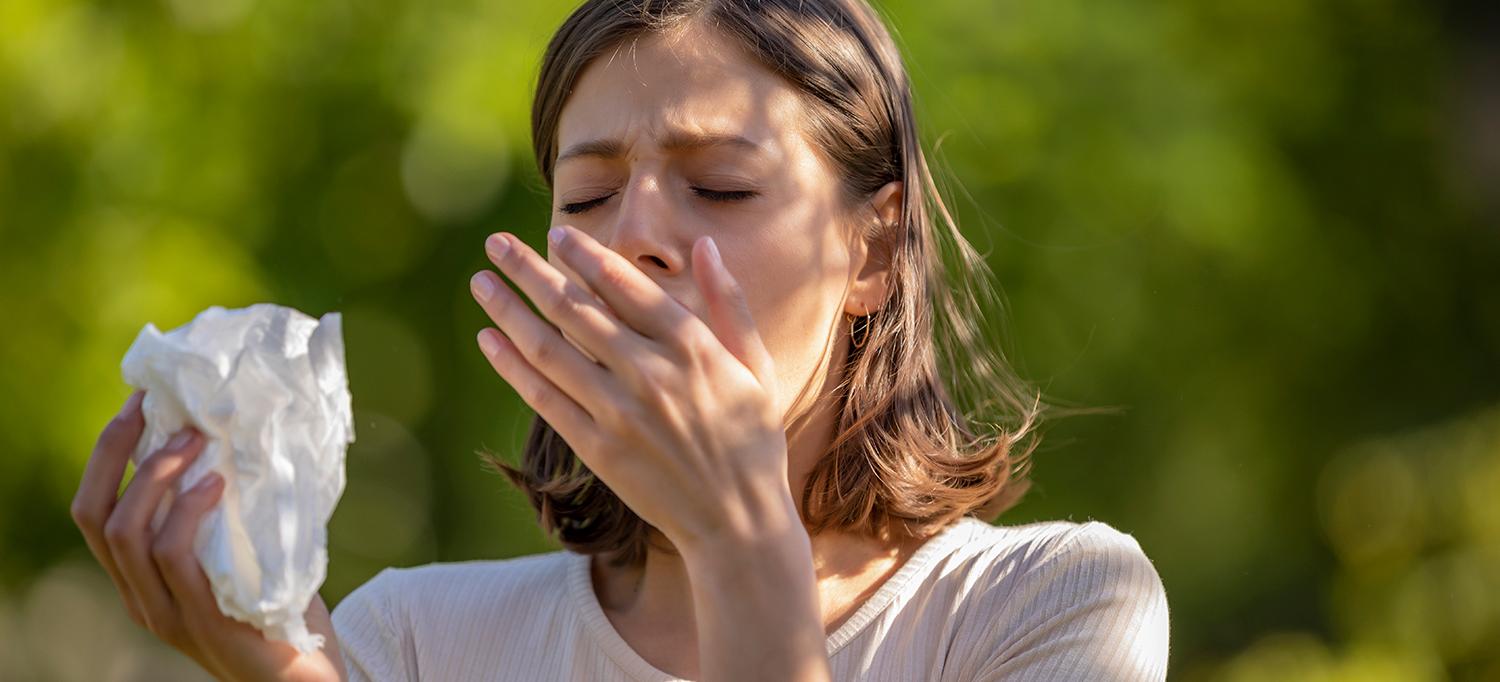 Woman in Park Sneezes While Holding a Tissue