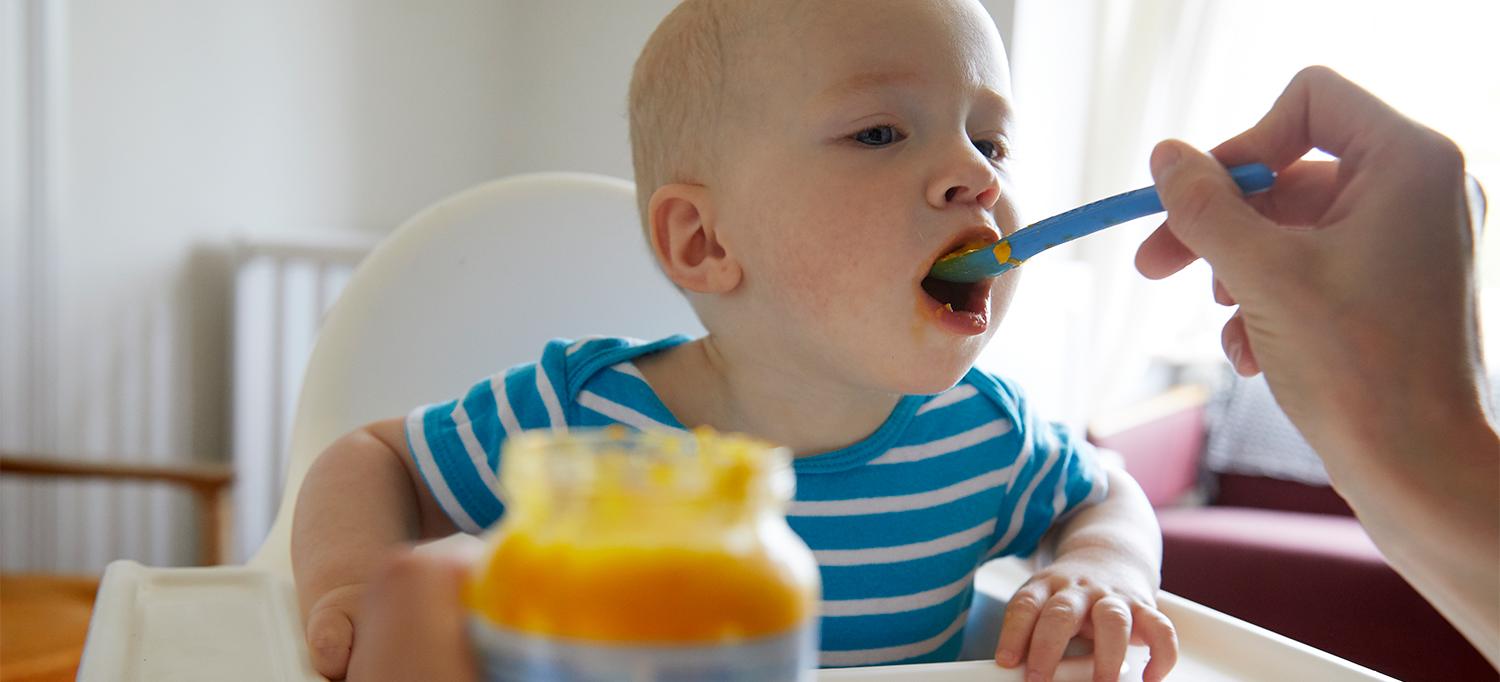 Person Feeding Young Child Baby Food from Jar