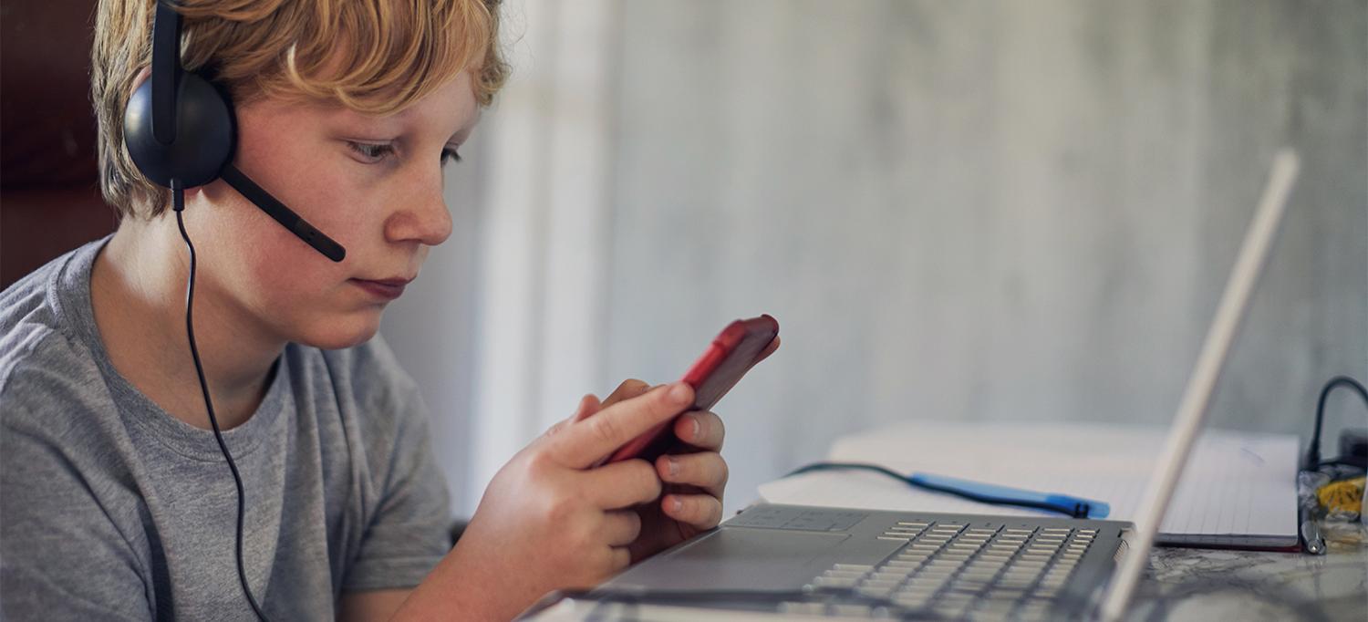 Kid Wearing Headphones Looking at Mobile Phone and Laptop Screens
