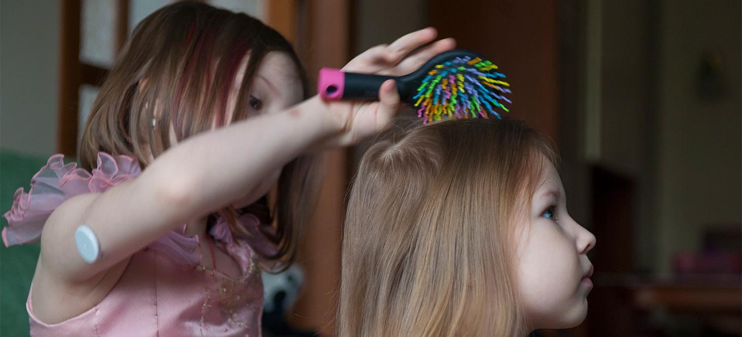 Child Wearing a Continuous Glucose Monitor Brushing Another Child’s Hair