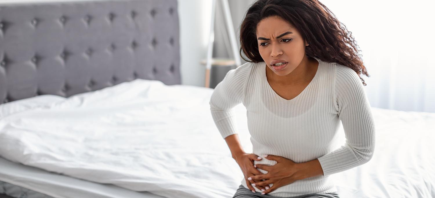 Woman Sitting on Bed Clutching Stomach