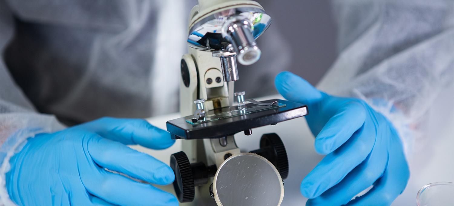 Person Wearing Personal Protective Equipment Examining Slide Under Microscope