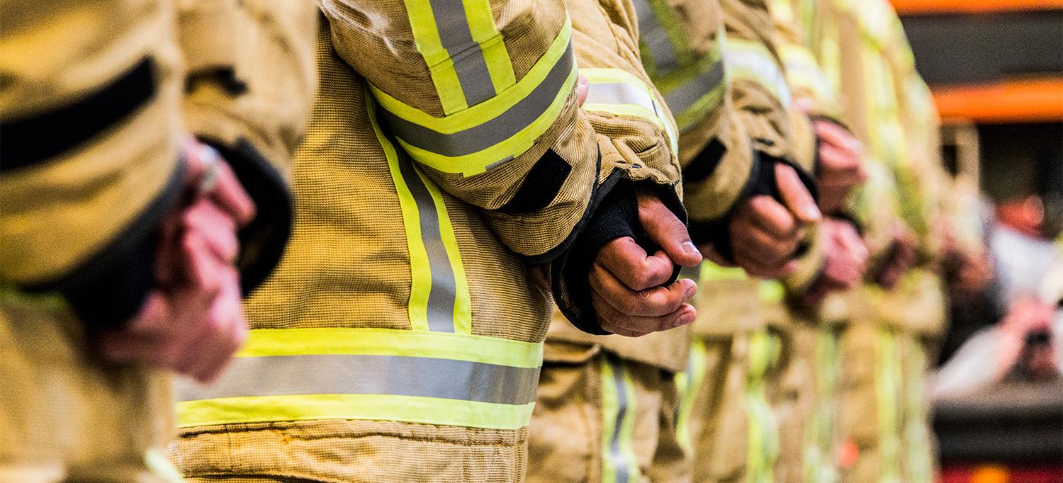 Firefighters Wearing Gear Standing in Row with Hands Behind Their Backs