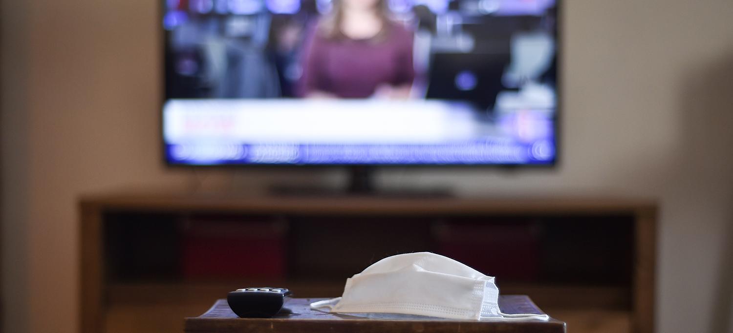 Face Mask and Remote on Table with TV on in Background