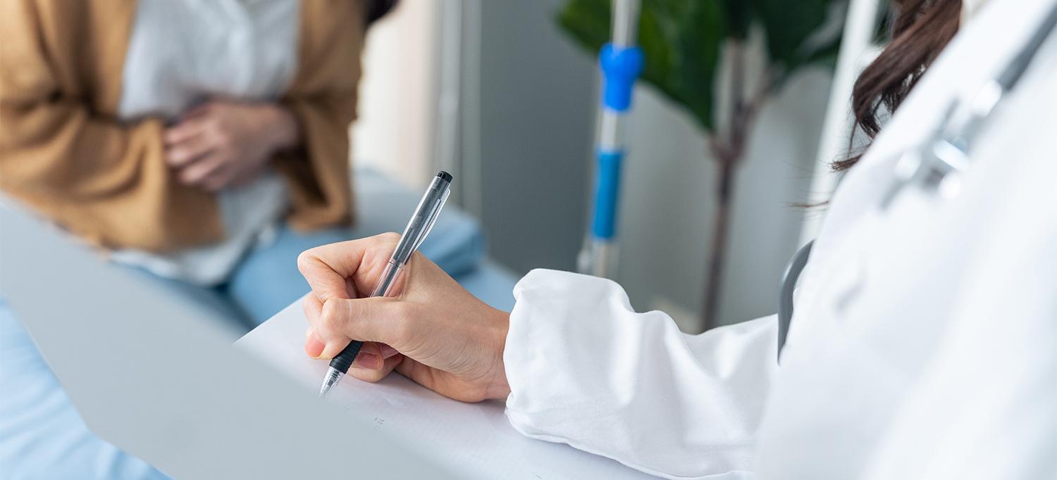 Doctor Taking Notes on Paper While Patient Clutches Stomach Next to Them