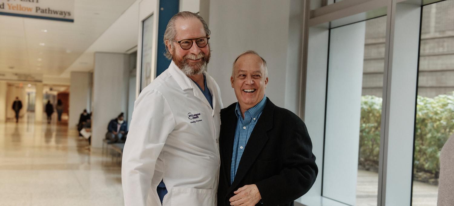 Dr. Robert Montgomery and Richard Capuano Smiling and Side Hugging in Hospital Hallway