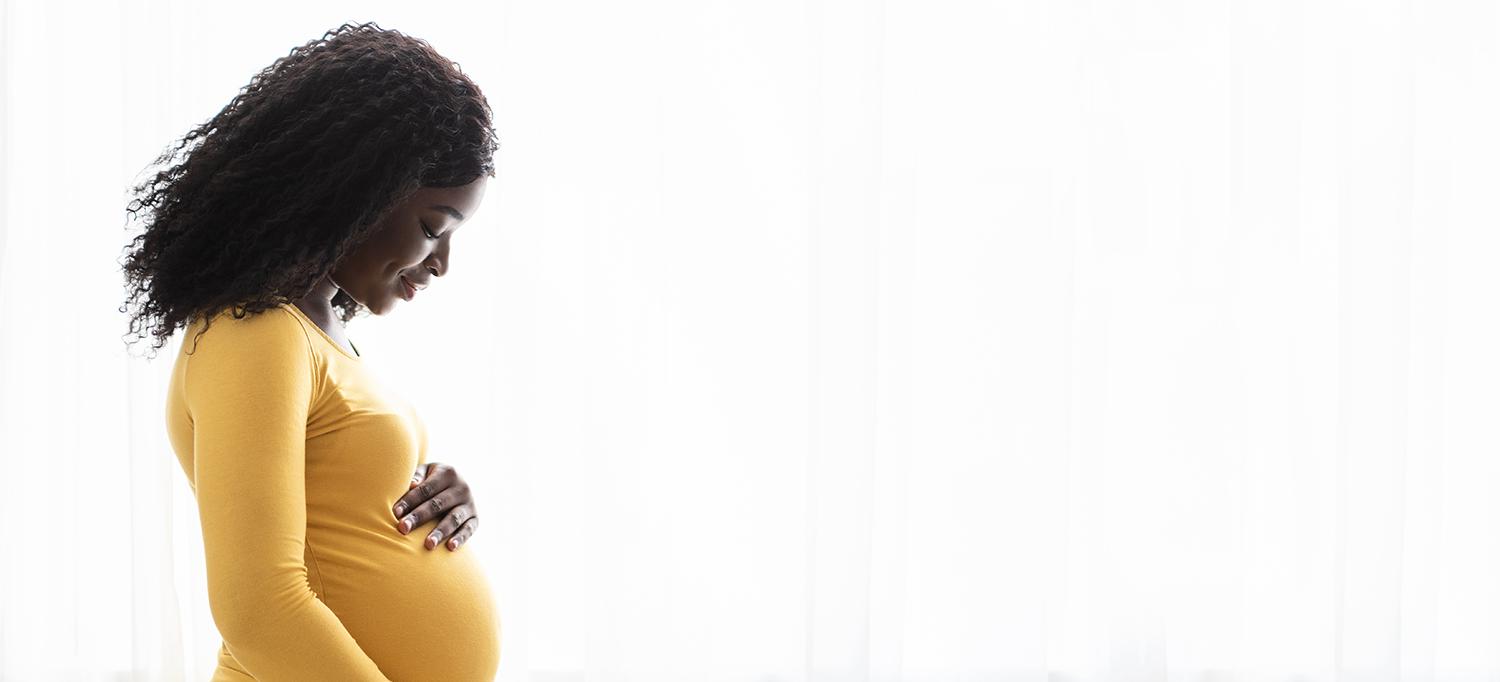 Visibly Pregnant Woman Stands with Arms Around Her Baby Bump
