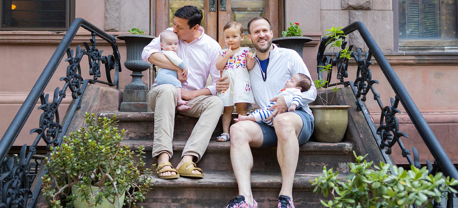 Sitting on a Stoop, David Turley Kisses His 5-Month-Old Son’s Forehead While Peter Thiede Holds Their Other Two Kids