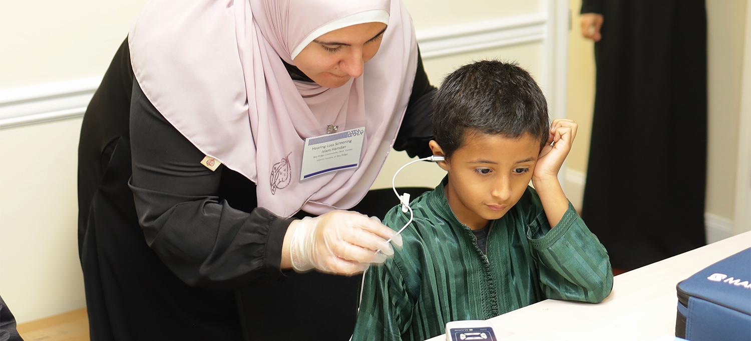 Woman leaning over small child to adjust the wire of the hearing device being used in the screening test