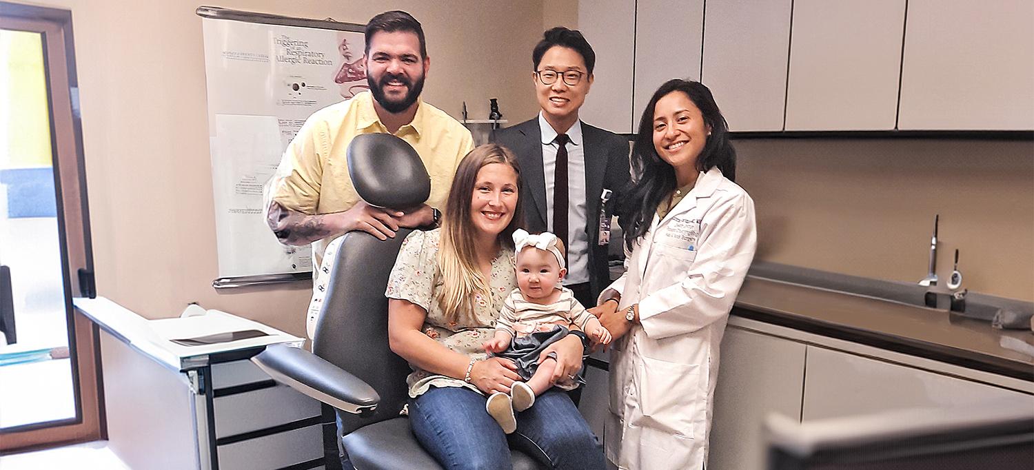 Kennedee sitting on her mom's lap in chair, with her dad, Dr. James G. Choi, and Dr. Zahrah Taufique standing behind them