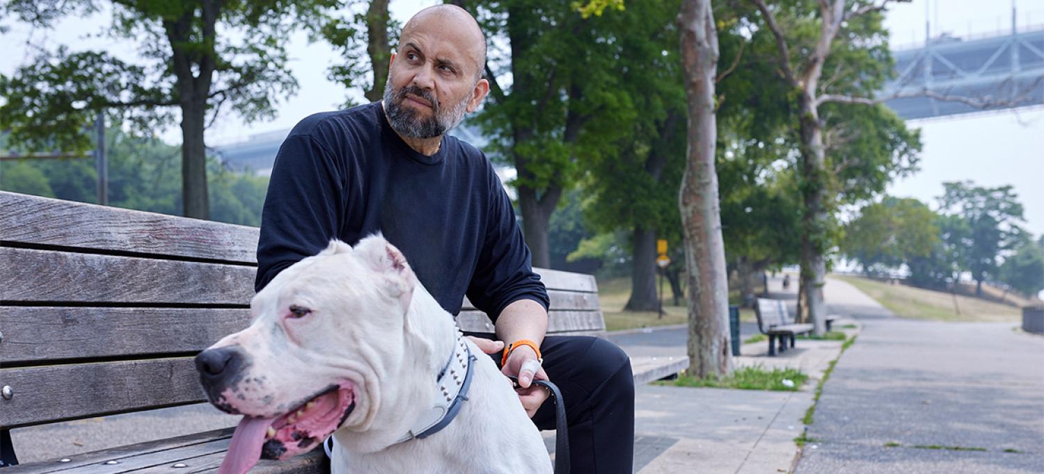 Joel Pretz sitting on a park bench, with mastiff Connor sitting on the ground near his feet and panting with his tongue out