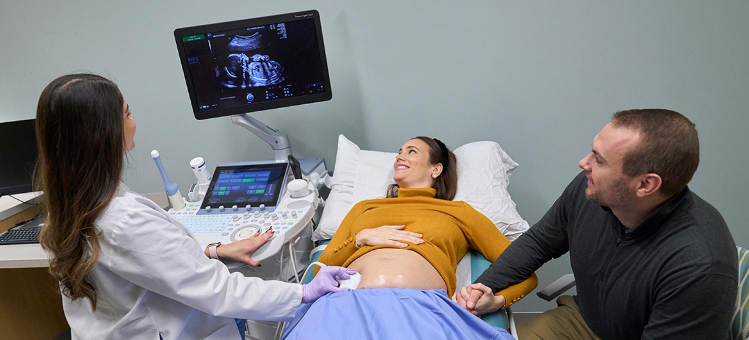 Healthcare provider performing ultrasound for pregnant woman who is accompanied by a partner in the exam room