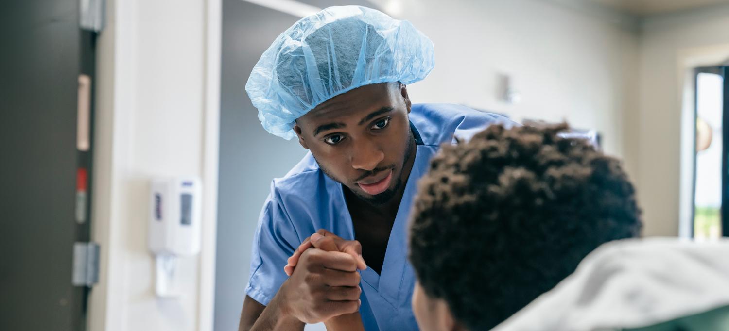 Black healthcare provider looking at and holding the hand of a Black patient in a hospital bed