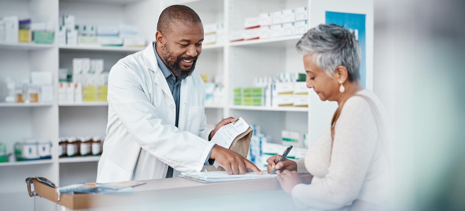 Smiling pharmacist helping patient complete forms attached to a clipboard on pharmacy counter