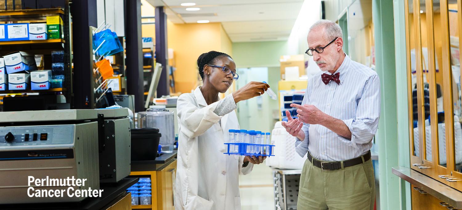 Dr. Jeffrey S. Weber assessing a test tube held up by colleague who is also holding a tray of more test tubes in lab