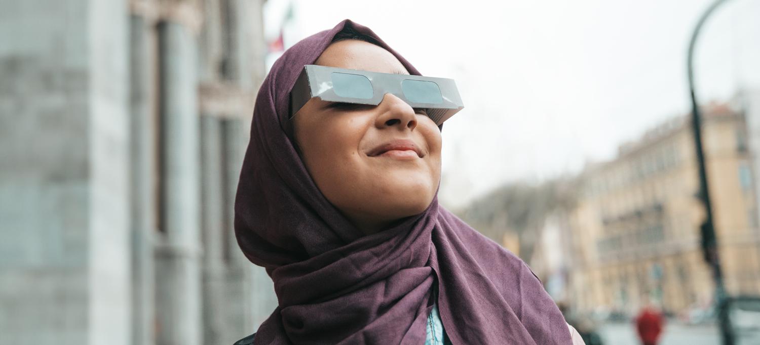 Person in city wearing protective eyewear and looking up at the sun