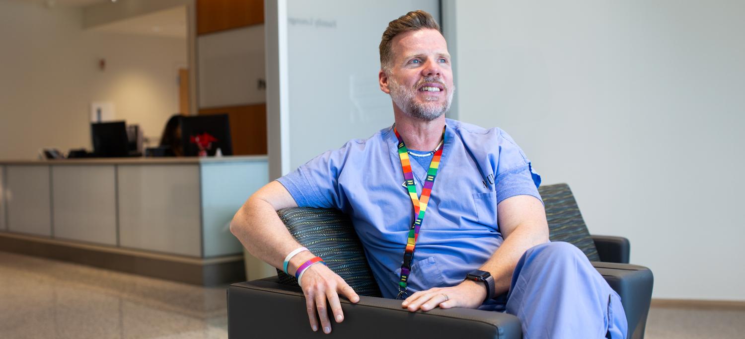 Kevin Moore wearing scrubs and a rainbow-colored lanyard, sitting in chair looking off camera