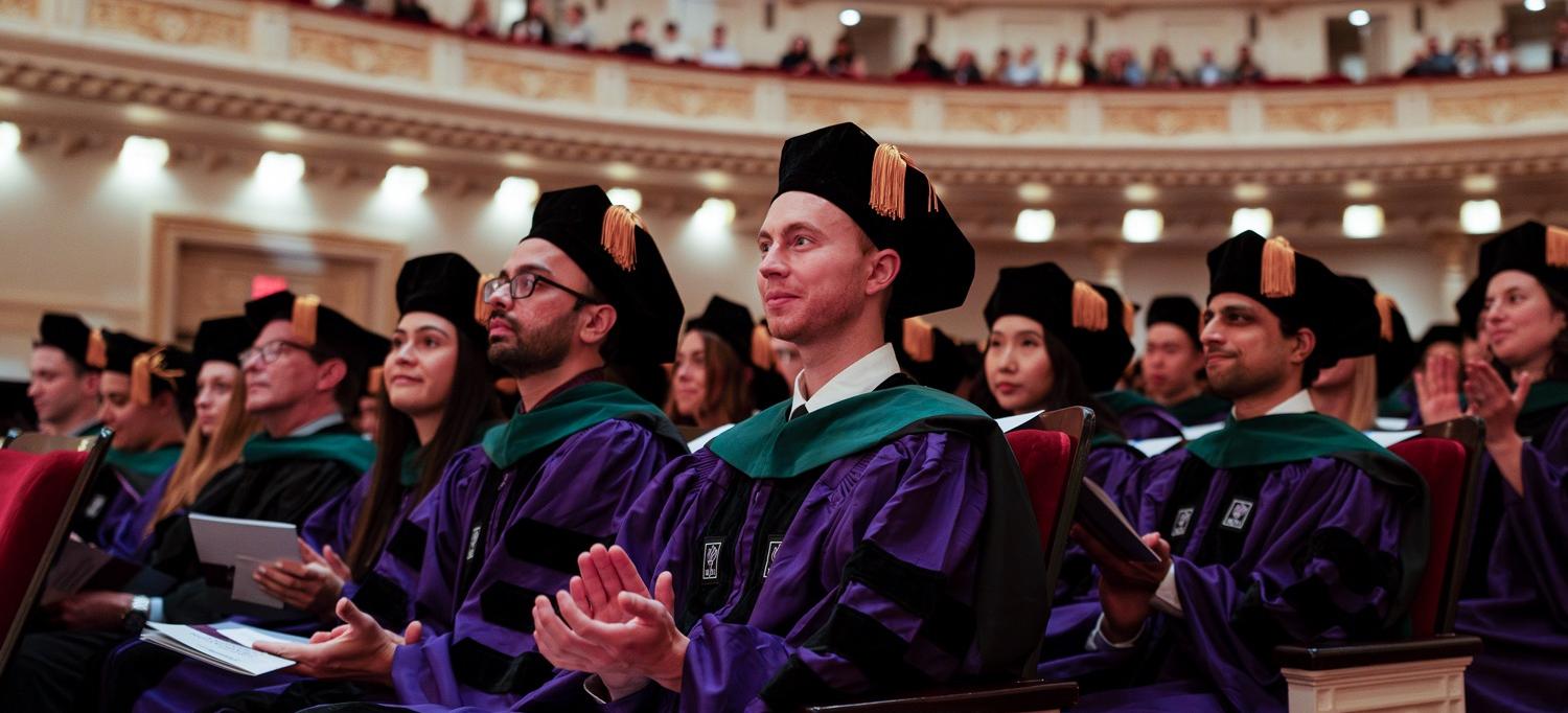 An auditorium filled with people in purple graduation robes and black graduation caps