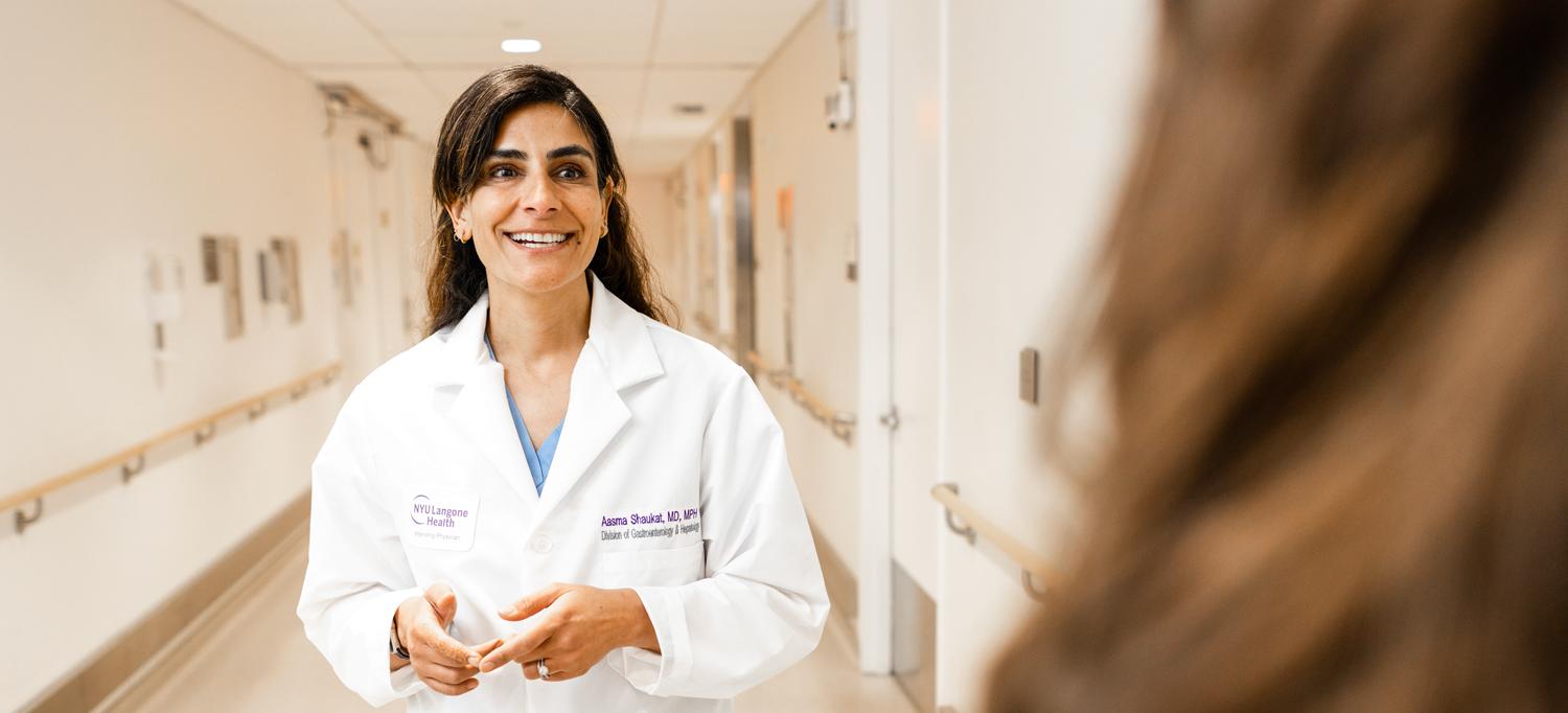Dr. Aasma Shaukat stands smiling in a hallway at NYU Langone.