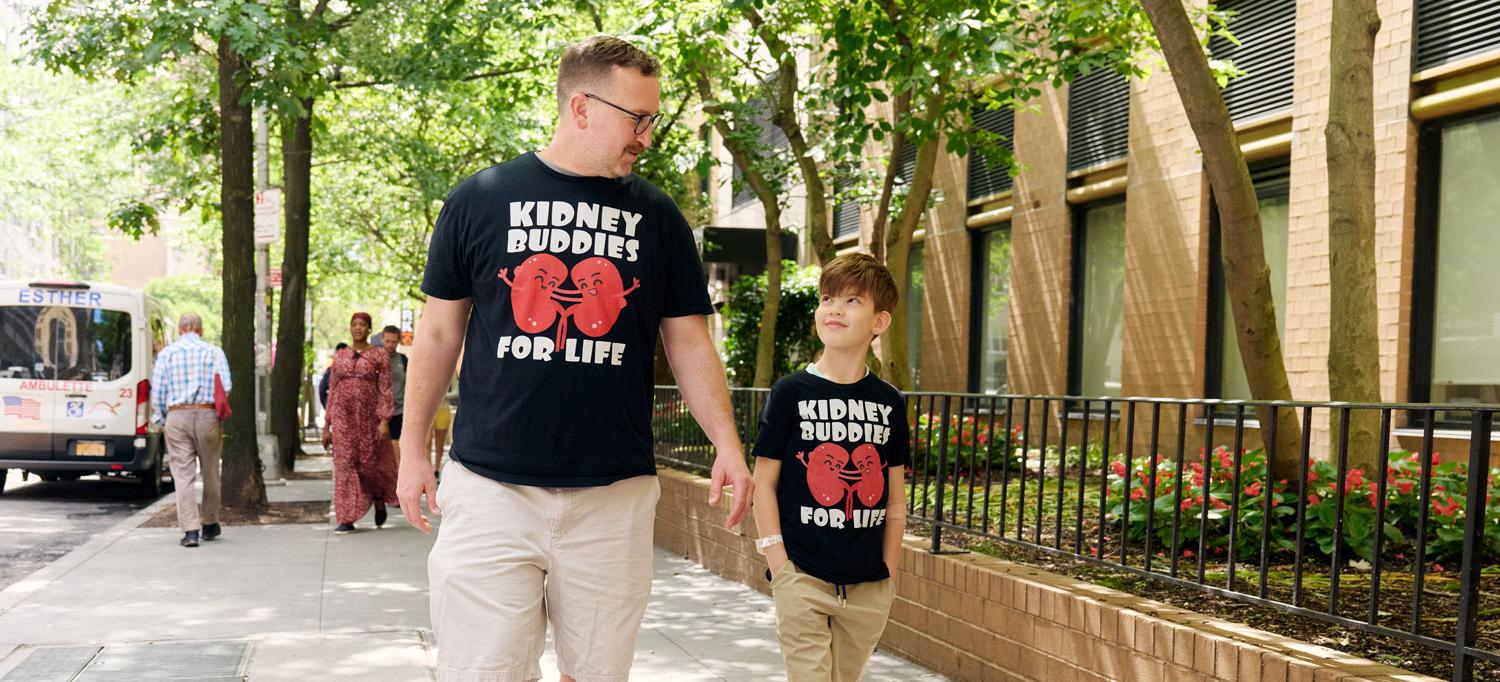 Wearing T-shirts that say “Kidney Buddies for Life,” Stephen and Jaren Munari walk together on the sidewalk.