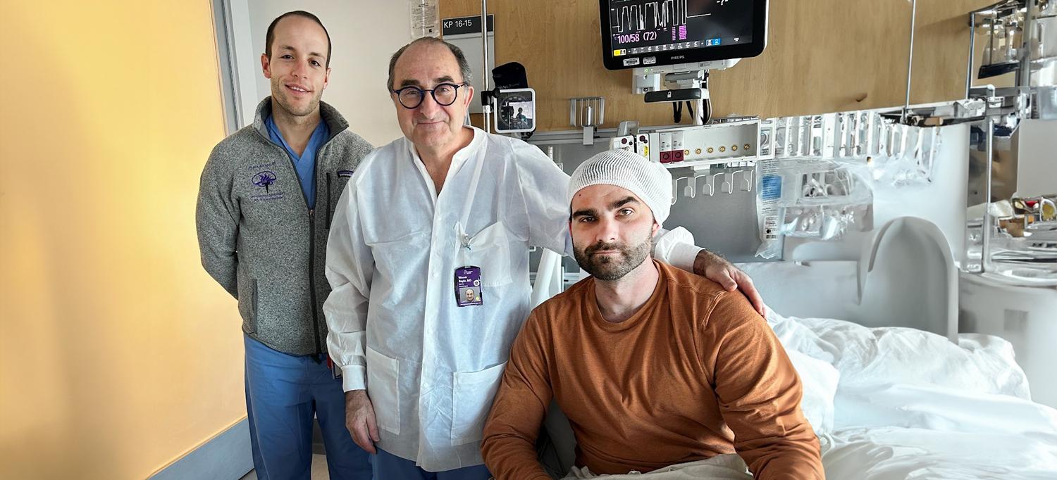 Dr. Rozman and Dr. Doyle stand next to Adamkiewicz, in a hospital bed.