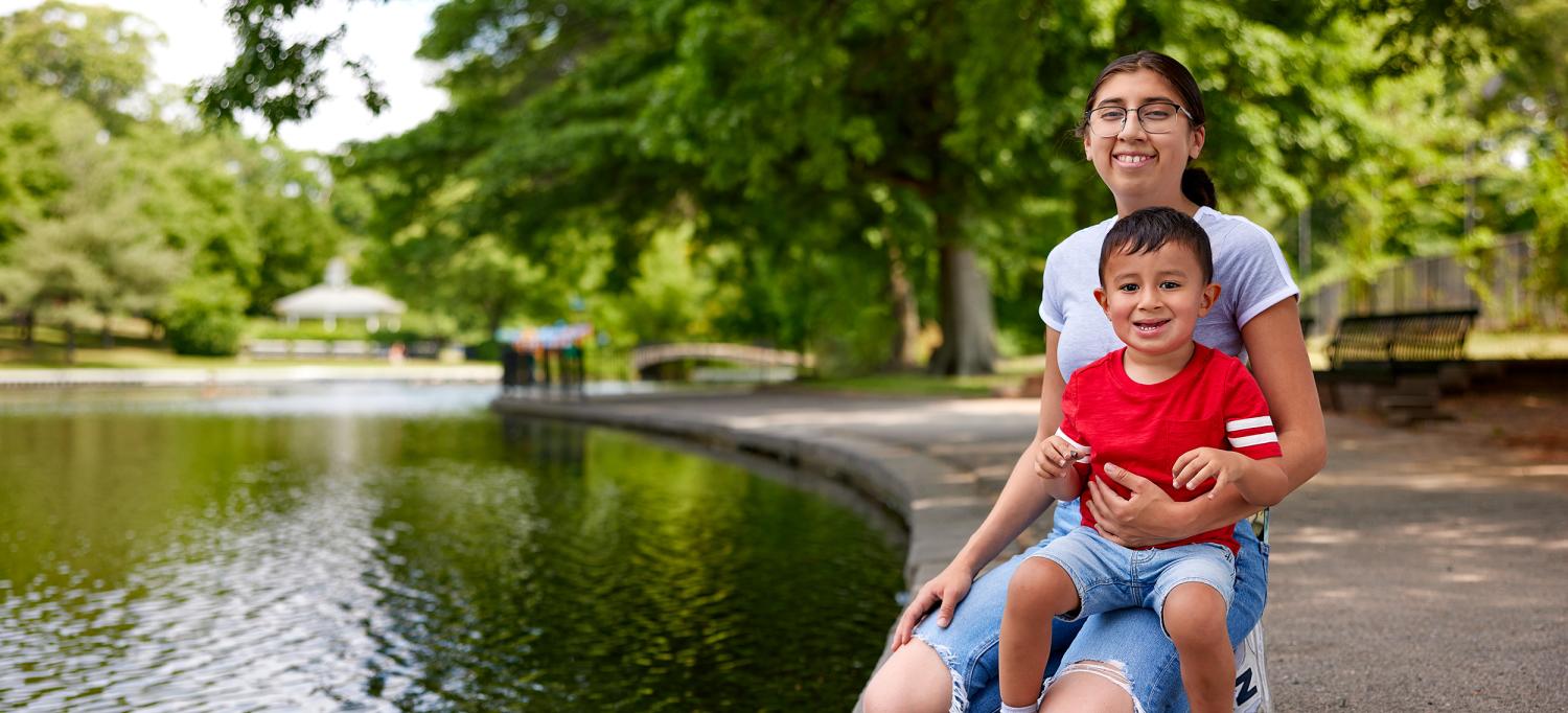 Alma and Malik sit smiling next to a park pond.