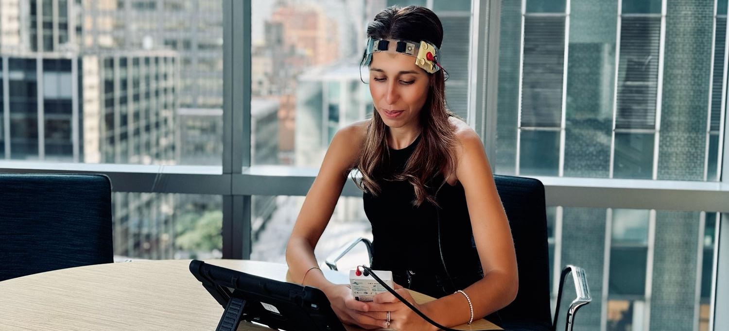 Dr. Pilloni sits at a desk wearing an electrical device around her head.