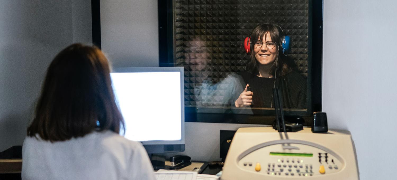 A patient wearing headphones takes a hearing test while smiling